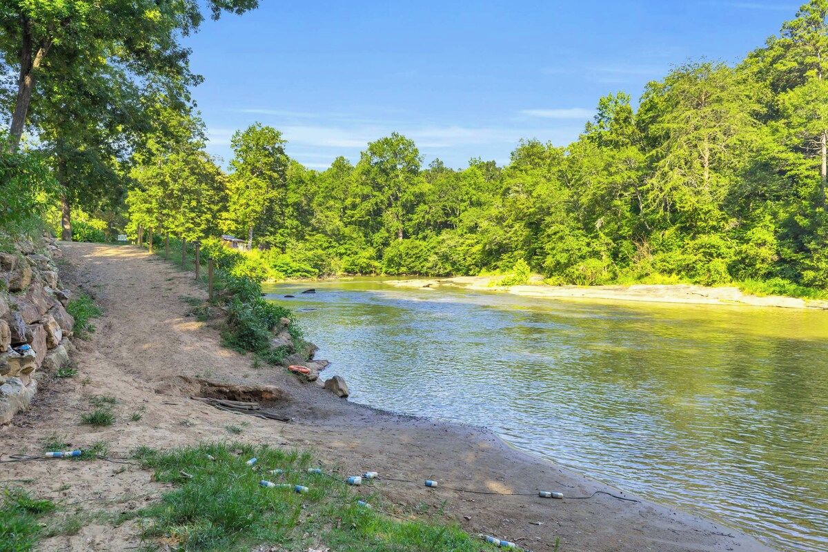 Ein Fluss mit einem Feldweg am Ufer, umgeben von dichtem Grün.