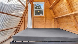 Una habitación pequeña en el ático, con una cama de metal y un ventanal.
