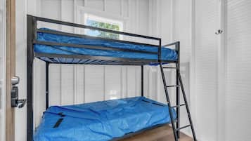 Una cama litera con un cubrecolchón azul, una escalera metálica y una pared blanca con paneles.