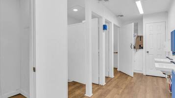 Un corridoio con pareti bianche e pavimento in legno, che conduce a un bagno con lavandino e specchio.