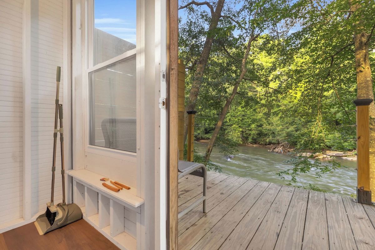 A wooden deck with a bench and a window overlooking a river.