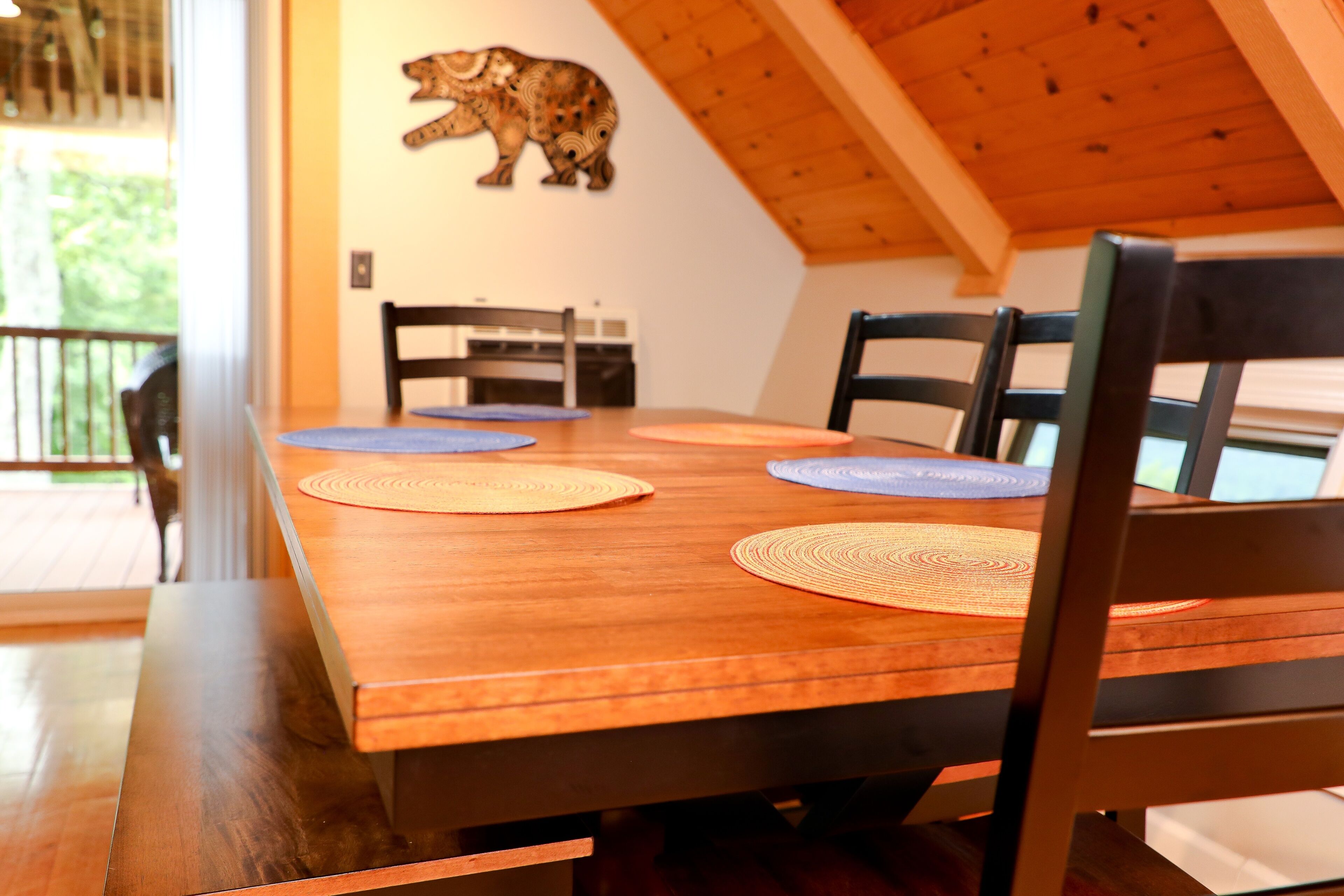 Una mesa de madera con cuatro sillas, un adorno de oso en la pared y vistas al exterior.