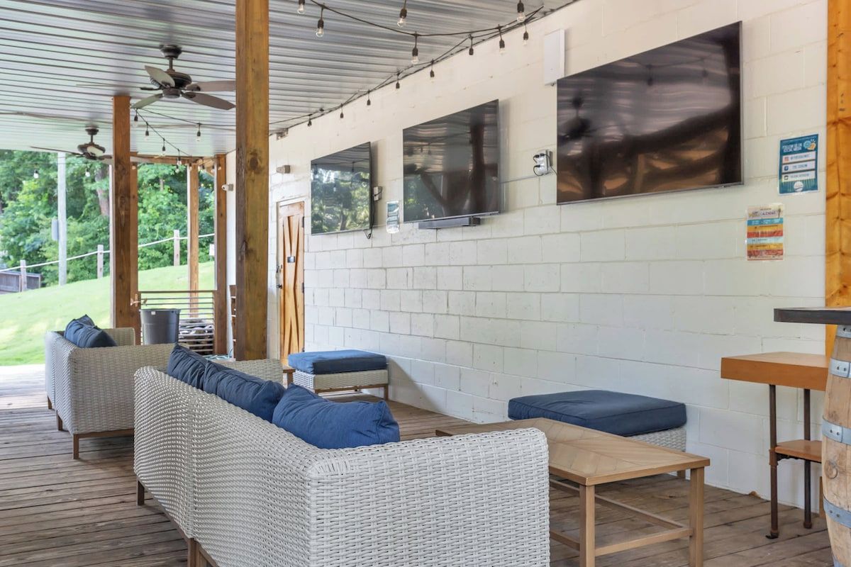 A covered outdoor seating area with wicker furniture and a flat-screen TV mounted on the wall.