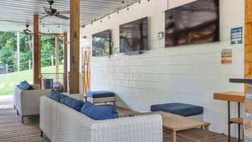A covered outdoor seating area with wicker furniture and a flat-screen TV mounted on the wall.