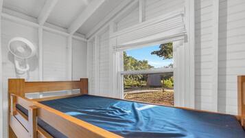 A single bed with a blue mattress in a room with white walls and a window.