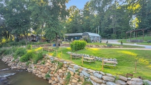 Un camping junto al río con mesas de picnic, un muro de piedra y cabañas.