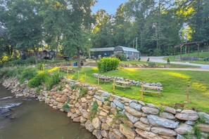 A riverside campsite with picnic tables, a stone wall, and cabins.