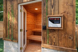 Puisesta laudeseinästä ja ohjauspaneelista koostuva sauna, jossa on kivipohja ja ovi.