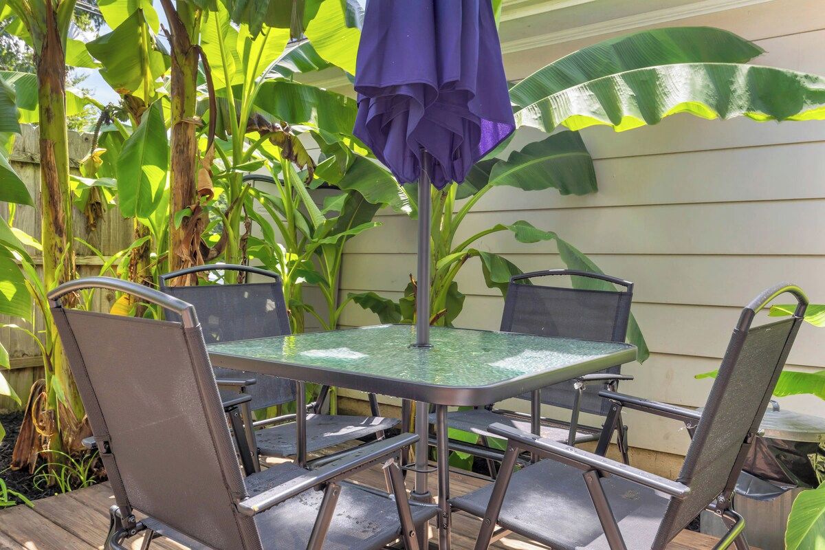A patio with a metal table and chairs, a purple umbrella, and large banana plants in the background.