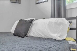 Ein Bett mit einer grauen gesteppten Decke, einem weißen Kissen und einem dunkelgrauen Kissen.