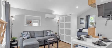 A modern living room with a grey sofa, a coffee table, and a dining area with white chairs and a table set for two.