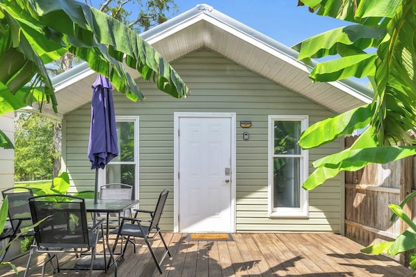 A house with a front door, a small patio with a table and chairs, and a wooden deck.