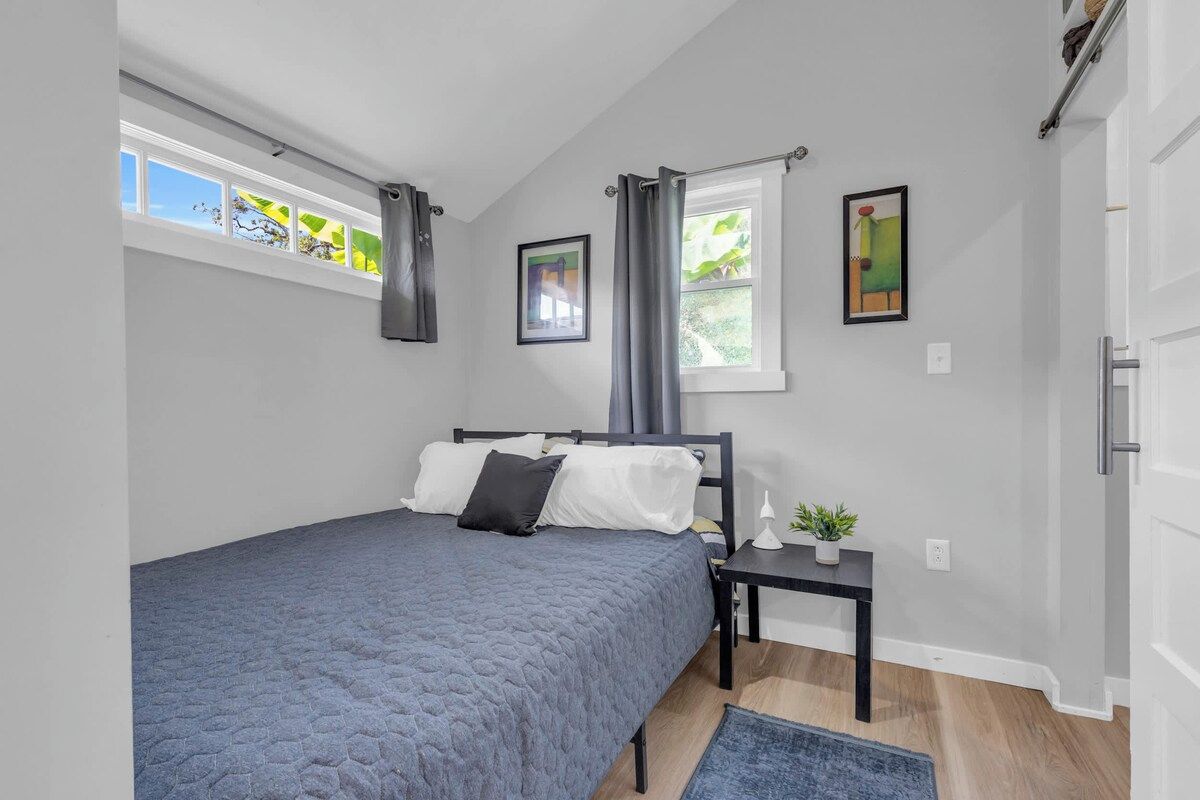 A bedroom with a bed, a nightstand, a window with curtains, and a wall-mounted picture.