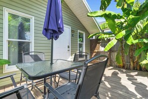 A patio with a glass table and chairs, a blue umbrella, and a wooden deck.
