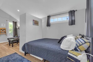 A bedroom with a bed, a window with curtains, a painting, and a view of the outdoors.