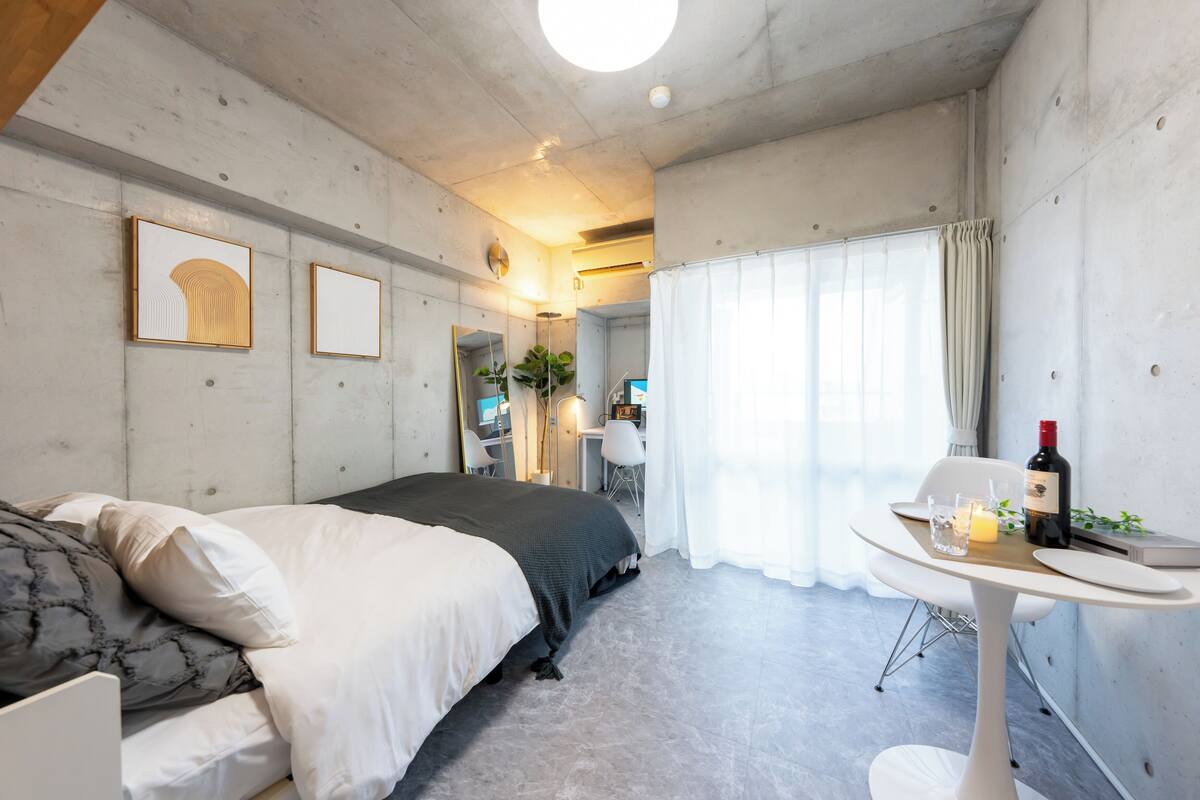 A modern bedroom with a bed, bedside table, and a small dining area with a table and chairs.