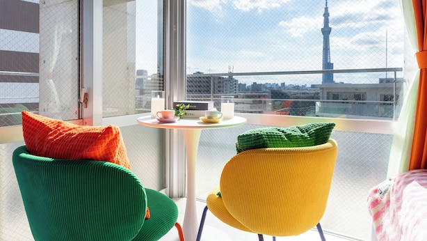 Un balcon avec deux chaises, une petite table sur laquelle se trouvent une tasse et une soucoupe, et une vue sur une tour.
