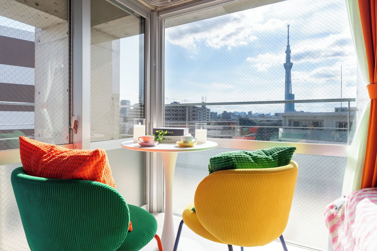 A balcony with two chairs, a small table with a cup and saucer, and a view of a tower.