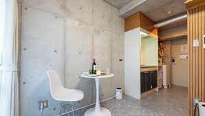 Une cuisine moderne avec un plan de travail blanc, une petite table ronde sur laquelle se trouvent une bouteille et des verres, et une chaise blanche.