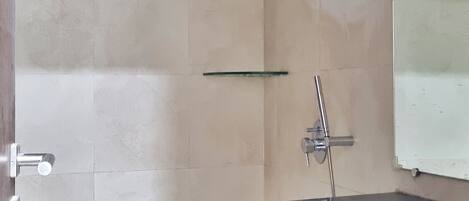 A bathroom with a shower, a glass shelf, a sink, and a mirror.