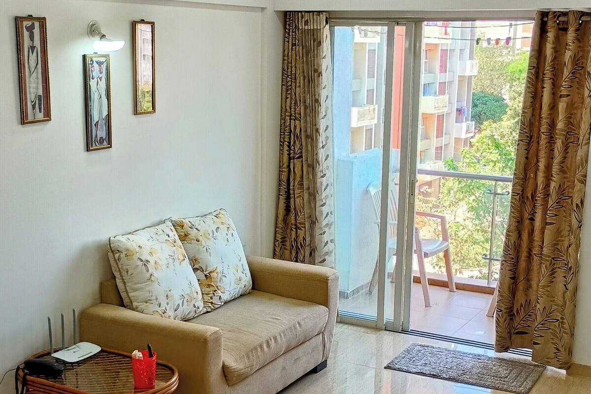 A living room with a sofa, a coffee table, a clock, and an air conditioning unit.