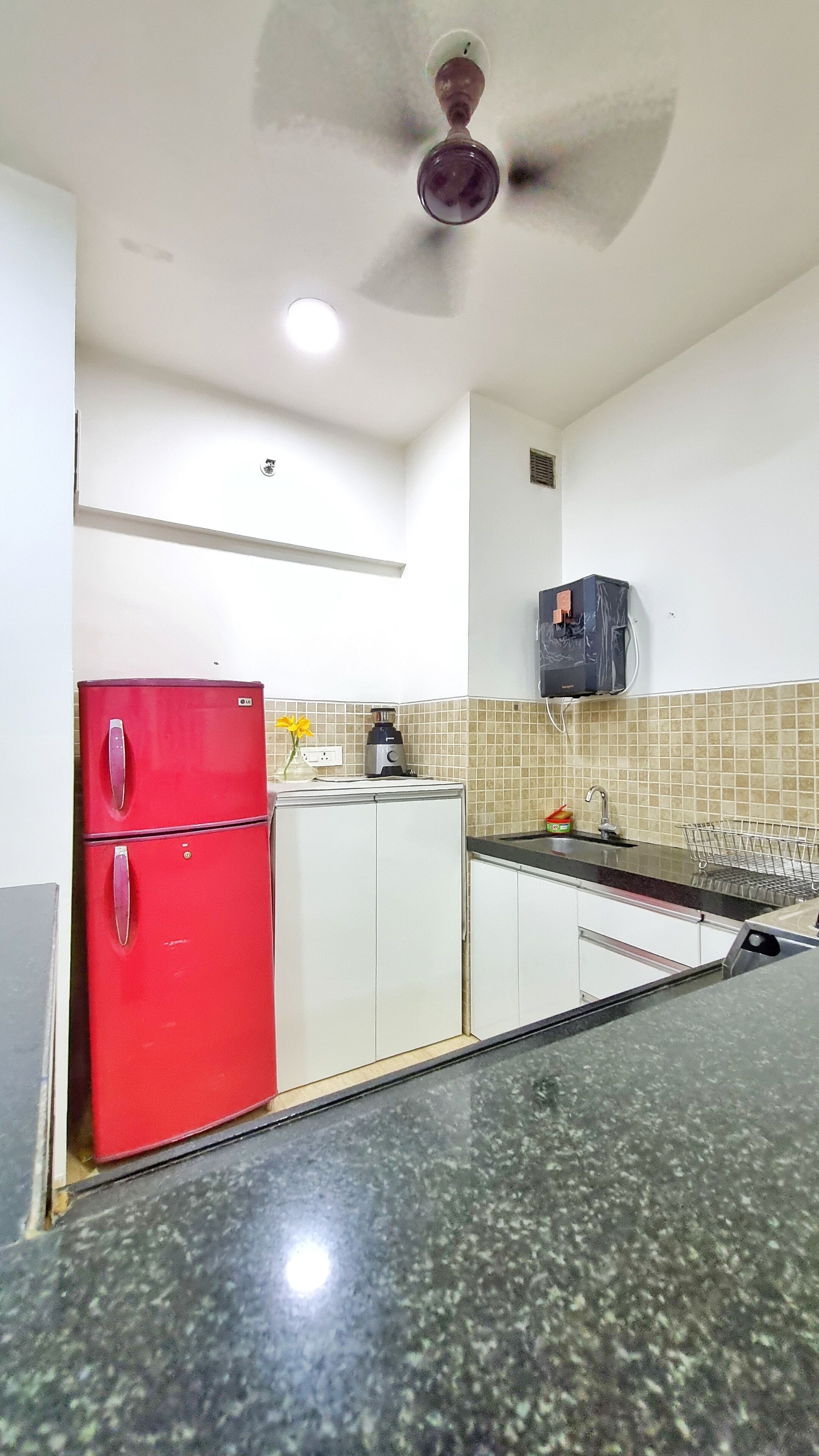 Een keuken met een rode koelkast, witte kasten, een zwart aanrecht en een plafondventilator.