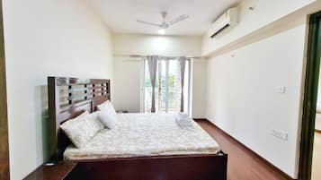 Un dormitorio con cama, ventilador de techo, equipo de aire acondicionado y ventana con cortinas.