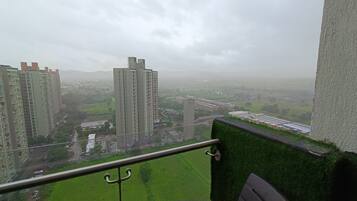 A high-rise building with multiple floors and balconies, overlooking a green landscape with fields and other buildings.