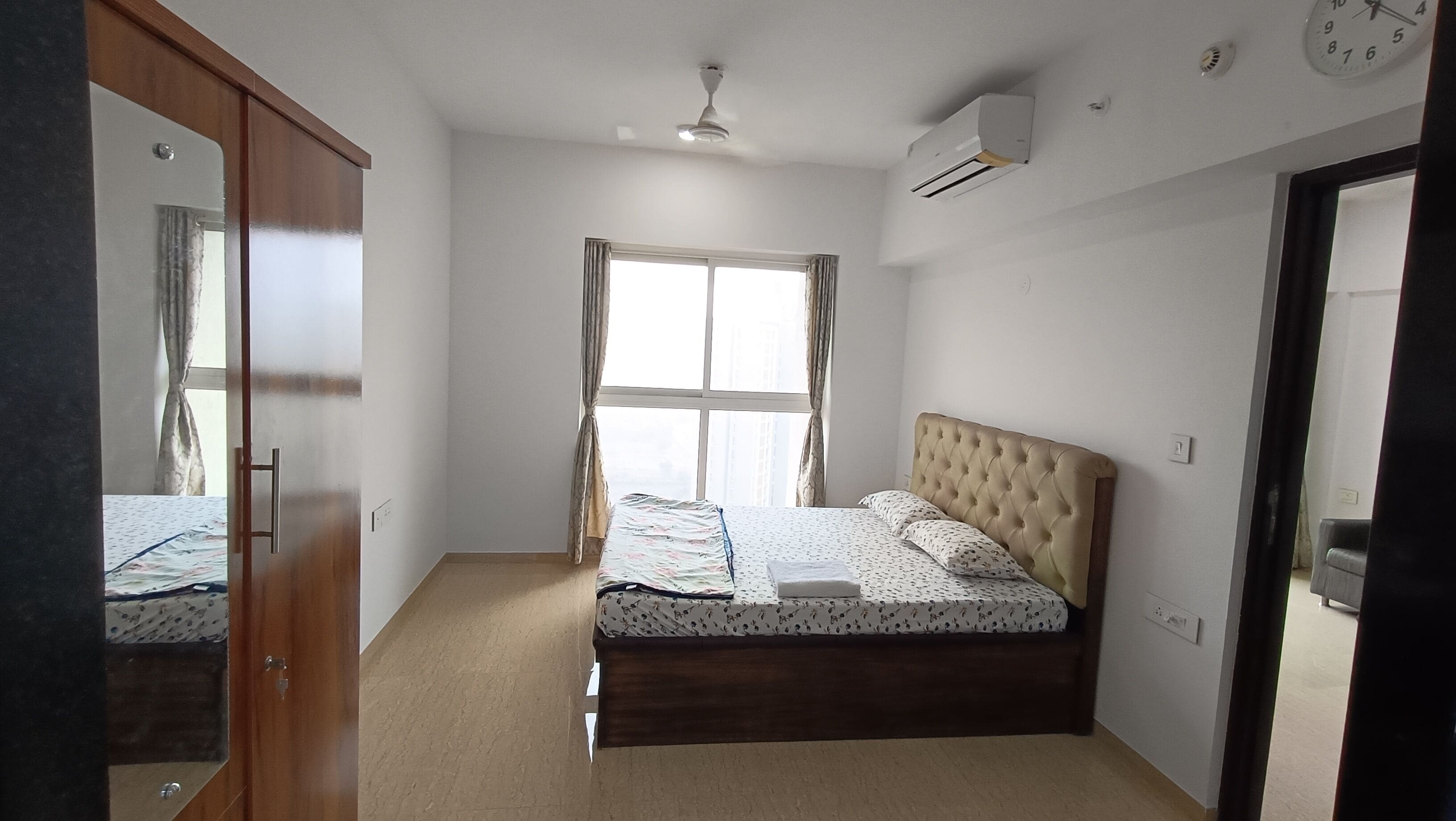 A bedroom with a bed, a wardrobe, a window, and an air conditioning unit.