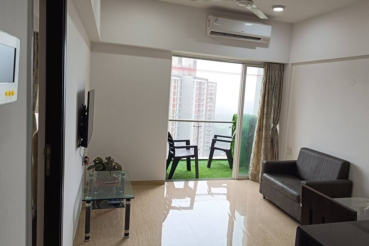 A modern living room with a glass coffee table, a sofa, and a balcony with chairs.