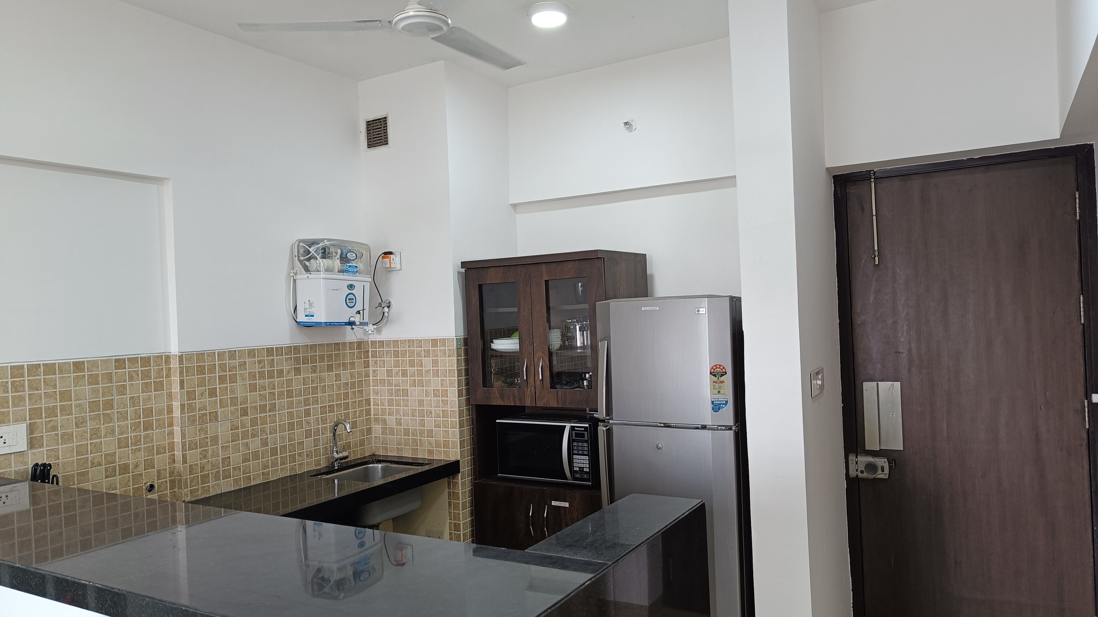A kitchen with a sink, a microwave, a refrigerator, and a water purifier.