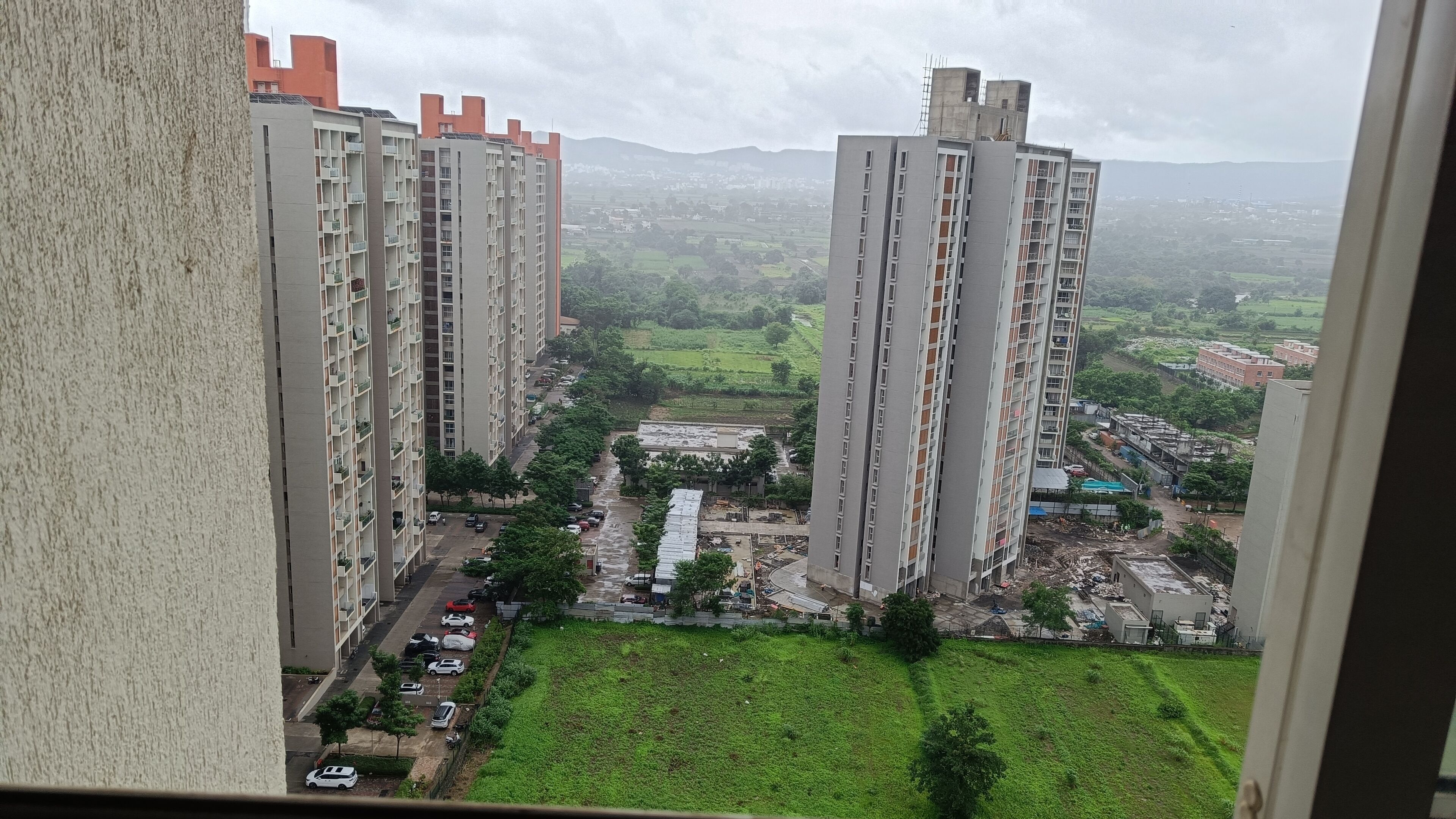 A high-rise building with multiple floors and balconies, surrounded by a green landscape and other buildings in the background.