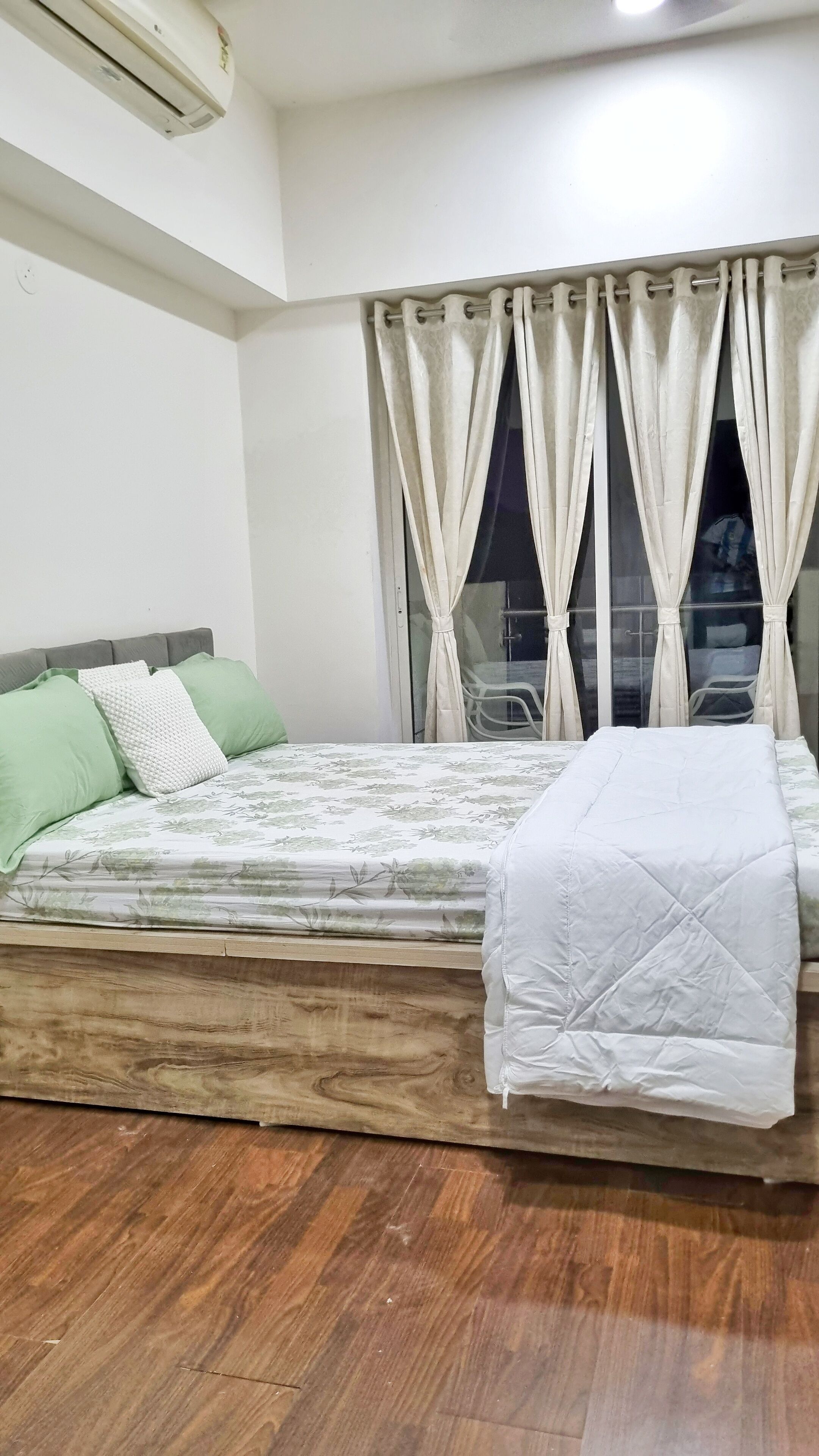 A bedroom with a bed, a window with curtains, a ceiling fan, and a wooden floor.