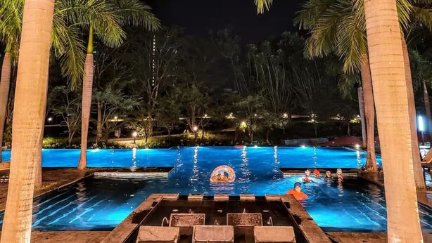 Ein Schwimmbeckenbereich bei Nacht mit Palmen und einem Wasserspiel.