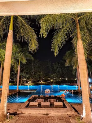 A nighttime swimming pool area with palm trees and a water feature. - Teesta Suites Lodha Belmondo Golf Resort (Mawal)