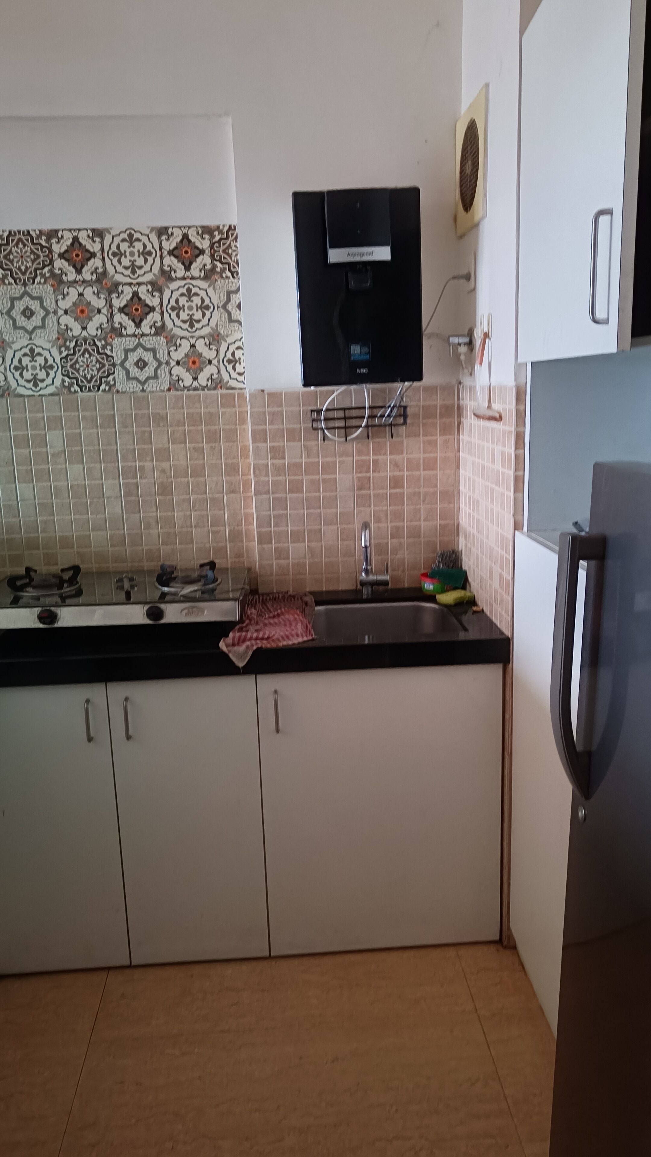 Eine Küche mit weißen Schränken, einer schwarzen Arbeitsplatte, einem eingebauten Herd, einer Spüle und einem kleinen Kühlschrank.