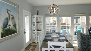 A dining area with a white table and chairs, a modern pendant light, and a painting of birds on the wall. - Ocean Lakes 920 | Ocean View + 4 King Beds | Sleeps 13 (Myrtle Beach)