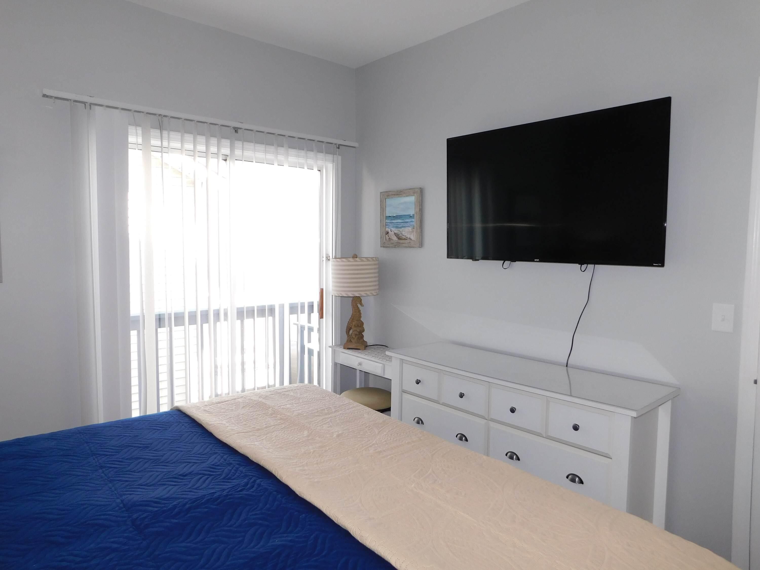 Ein Schlafzimmer mit Bett, Fernseher, Schreibtisch und einem Fenster mit Vorhängen.