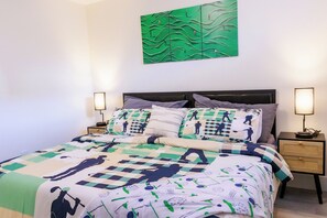A neatly made bed with a patterned bedspread, two bedside tables with lamps, and a green abstract painting on the wall. - Elegant Modern Loft in Prestigious Fairways (Riverview)