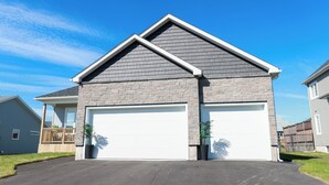 A two-story house with a garage, a stone facade, and a clear blue sky. - Elegant Modern Loft in Prestigious Fairways (Riverview)