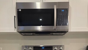 A kitchen with stainless steel appliances, including a microwave, oven, and stovetop. - Elegant Modern Loft in Prestigious Fairways (Riverview)