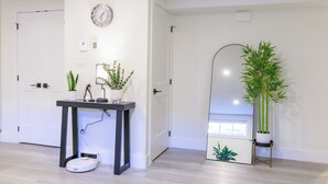 A modern living room with a minimalist design, featuring a round wall clock, a small table with a potted plant, a standing plant, and a robotic vacuum cleaner. - Elegant Modern Loft in Prestigious Fairways (Riverview)