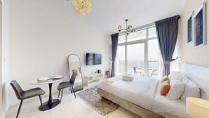 A modern hotel room with a large bed, a desk with a chair, a TV, and a balcony with a view.
