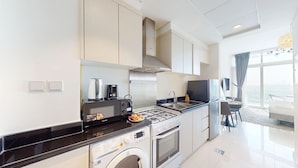 A modern kitchen with a gas stove, microwave, and built-in oven. There is a sink and a dining area with a view of the sea.