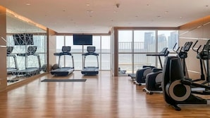 A spacious gym with treadmills, elliptical machines, and a large window offering a city view.