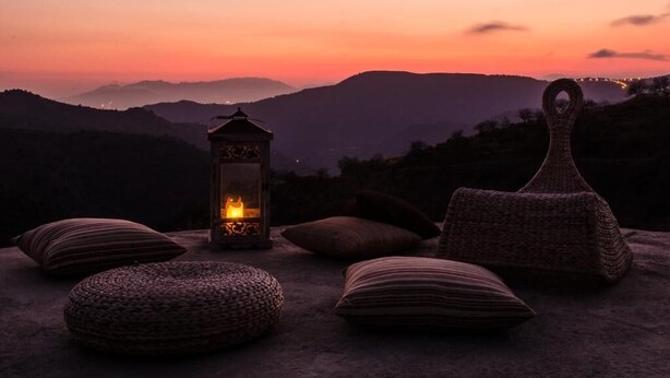 Une vue sur le coucher de soleil, avec une lanterne, des coussins et un panier tressé posés sur une surface.