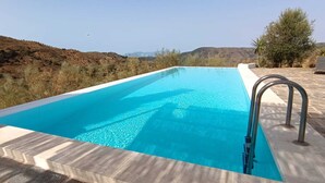 Une piscine rectangulaire à l’eau d’un bleu limpide, entourée d’une terrasse en pierre et dotée d’un escalier en métal.