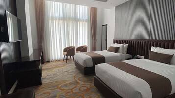 A hotel room with two beds, a flat-screen TV, a desk, and a large window with curtains.
