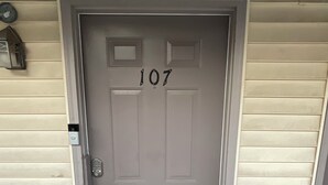 Una porta gris amb el número 107, una closca de correu i un graó petit que condueix a la porta.