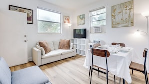 Ein modernes Wohnzimmer mit einem weißen Sofa, einem Esstisch für zwei Personen und Kunstwerken an den Wänden.